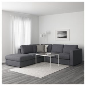 Modern living room with a gray sectional sofa, white walls, sheer curtains, and a framed black-and-white photo on the wall near a white lamp fixture on the wall/standarike edge of the sofa area.