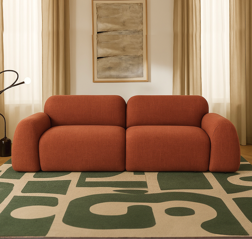 Two-section orange sofa in a neutral living room with a geometric green rug and beige curtains on either side.