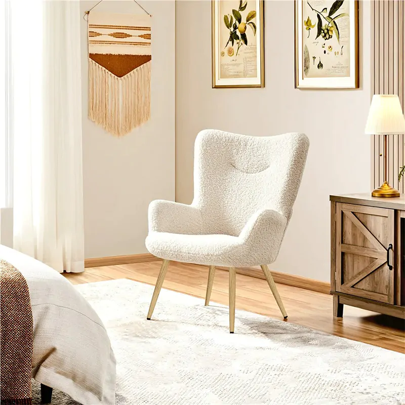 White boucle armchair with wooden legs in a cozy bedroom/living area next to a wooden cabinet and lamp, with botanical prints on the wall and a textured rug.