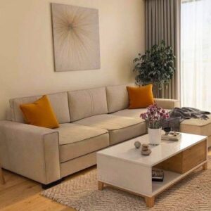 Beige sofa with orange cushions in a bright living room, white coffee table, and a tall plant nearby.